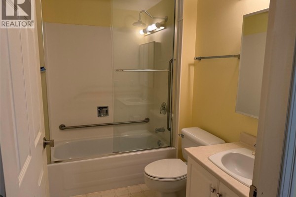Bathroom with a white tub, glass shower doors, toilet, and vanity. - 204 2045 Carrick St, Oak Bay