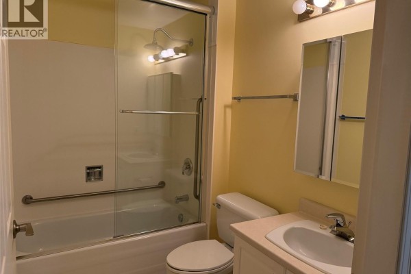 Bathroom with a white tub, glass shower doors, toilet, and vanity. - 204 2045 Carrick St, Oak Bay