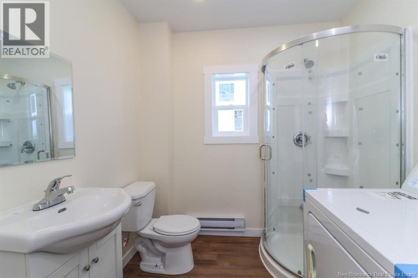 Compact bathroom with a white vanity, toilet, and a curved glass shower stall. - 204-206 St. James W Street, Saint John