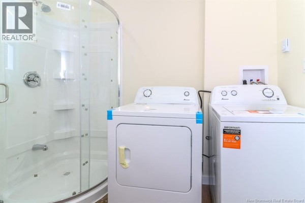 View of a shower stall and two white laundry machines in a bathroom. - 204-206 St. James W Street, Saint John