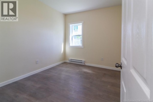 Empty bedroom with cream walls, a small window, and dark wood-look flooring. - 204-206 St. James W Street, Saint John