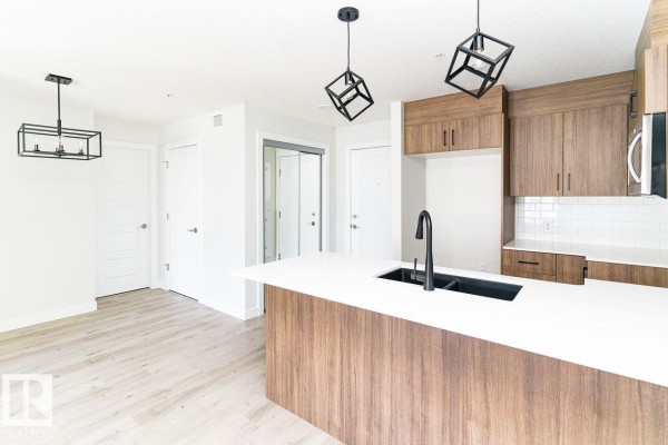 Corner kitchen with wood cabinetry, white countertops, black sink, and modern pendant lighting. - #204 2225 44 Av Nw, Edmonton