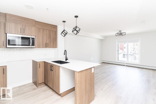 Open concept kitchen and living area with light wood flooring and white walls. - #204 2225 44 Av Nw, Edmonton