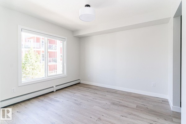 Living room with a large window, light wood flooring, and a view of trees and buildings. - #204 2225 44 Av Nw, Edmonton