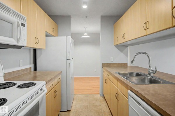Kitchen with light wood cabinets, beige countertops, white appliances including refrigerator and stove, and a sink. - #204 2430 Guardian Rd Nw, Edmonton