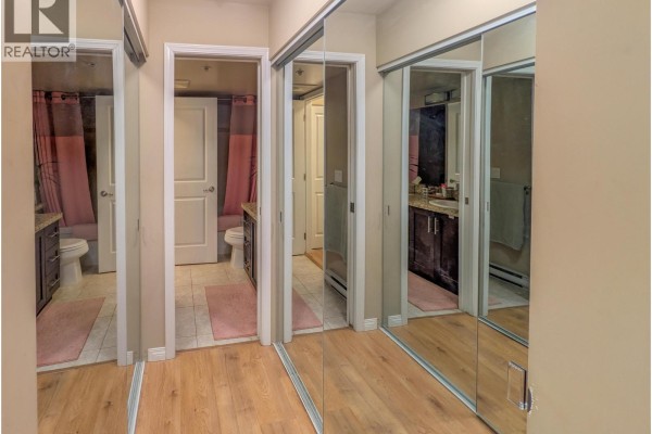 Hallway with mirrored closet doors reflecting two doorways, one leading to a bathroom with a pink shower curtain. - 204 5000 Imperial Street, Burnaby