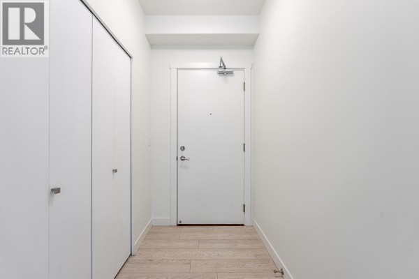 Interior hallway with white walls, a white door, and light wood flooring. - 204 711 W 14th Street, North Vancouver
