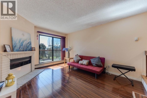 Living room with red sofa, fireplace, and large window overlooking balcony - 204 8511 Westminster Highway, Richmond