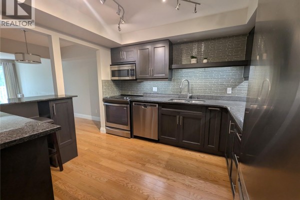 Open kitchen with dark cabinetry, stainless steel appliances, and breakfast bar - 204 921 Main Street E, Saskatoon
