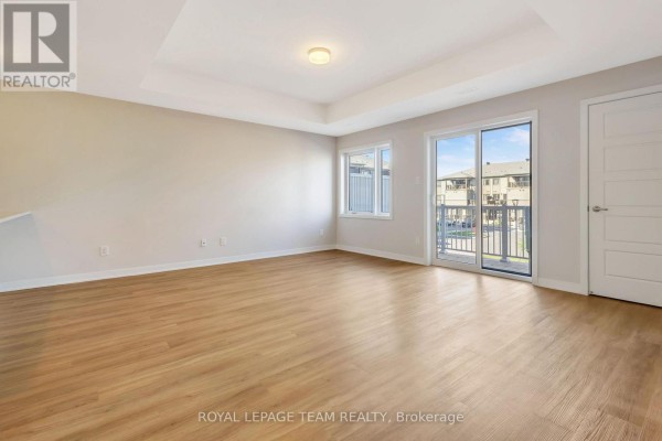 Spacious living room with light wood laminate flooring and patio doors to a balcony. - 204 Lillian Freiman Private, Ottawa