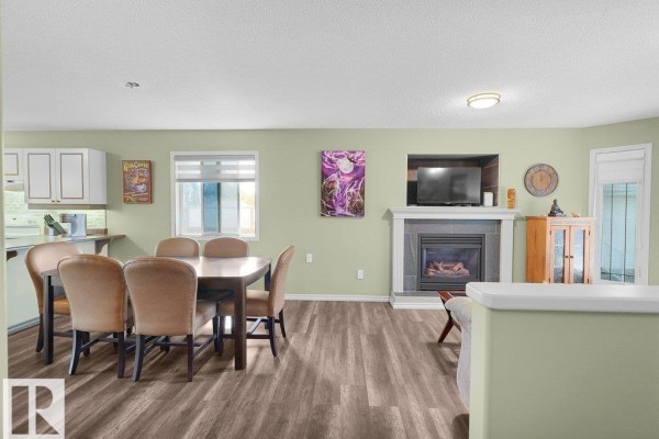 Open concept living and dining area with light green walls, dark wood floors, fireplace, and dining table. - 204 Westmews Dr Nw, Fort Saskatchewan