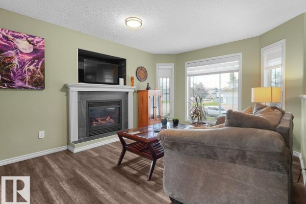 Living room with light green walls, dark wood floors, fireplace, couch, coffee table, and large window. - 204 Westmews Dr Nw, Fort Saskatchewan