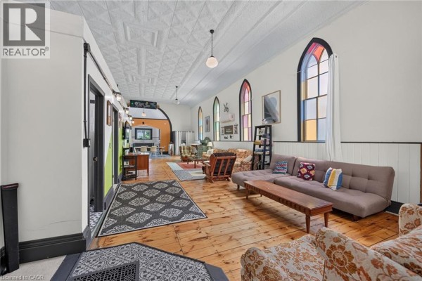 Interior living space with original wood floors, tall arched windows, and a long sectional sofa. - 2040 Main Street, Walsingham