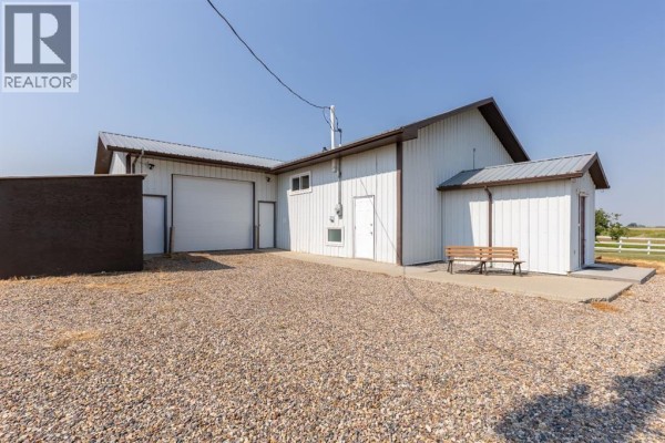 Aerial view of a rectangular property with a white metal building, gravel driveway, and lawn. - 204004 Twp Rd 6-4, Raymond
