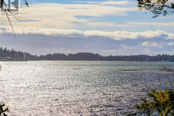 Side view of the house with a patio area, surrounded by trees and water access. - 2042 Glenidle Rd, Sooke