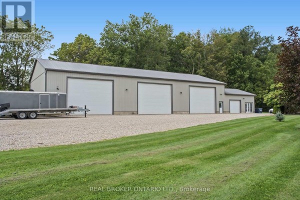 Rear view of the brick ranch house showing a garage, landscaping, and a fence on a gravel driveway. - 204364 Keswick Road, South West Oxford