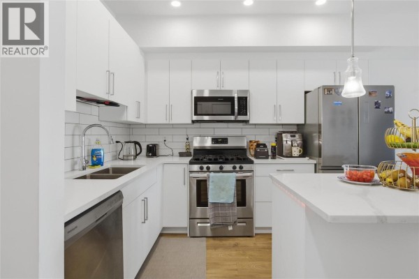 White kitchen featuring white subway tile backsplash, stainless steel appliances, and quartz countertops. - 2046 Robson Place Unit# 216, Kamloops
