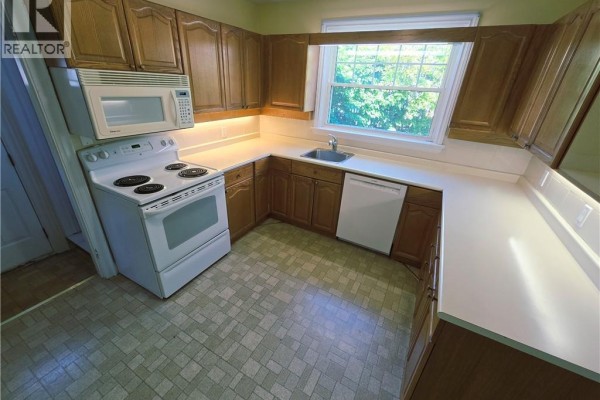 Corner view of a kitchen featuring light wood cabinetry, white countertops, and a window overlooking greenery. - 2047 James Street, Burlington