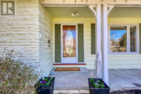 Front porch entrance with a glass-paned door, white columns, and potted plants. - 2048 Devon Road, Oakville