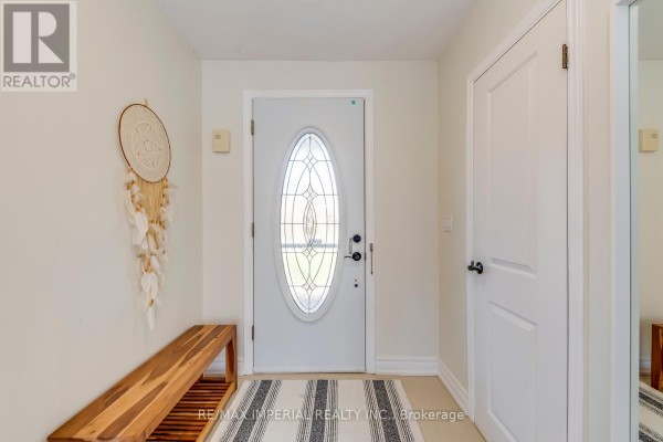 Interior entryway with a white door, a wooden bench, and a decorative wall hanging. - 2048 Devon Road, Oakville