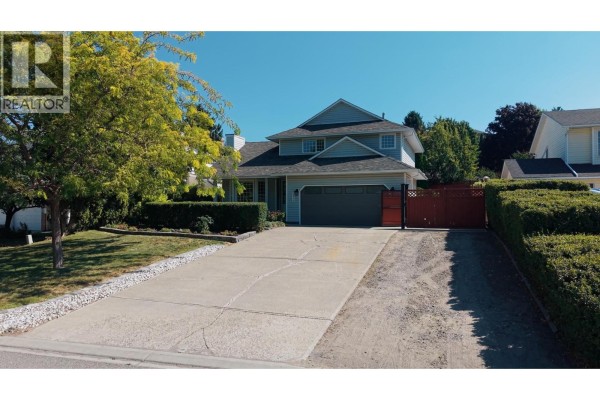 Aerial view of the driveway leading to a grey house with a double garage, surrounded by green lawn and hedges. - 2049 Tremerton Drive, Kamloops