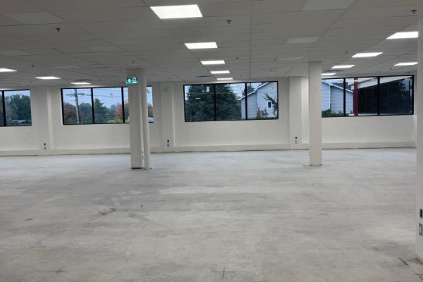 Unfinished commercial interior with concrete floor, white walls, and windows showing outdoor trees. - 205 - 31 Northside Road, Ottawa