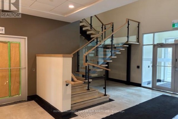 Modern staircase with wood treads, glass panels, and metal railings in a commercial building lobby. - 205 - 35 Sunday Drive, Aurora