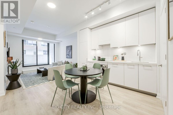 Kitchen with white cabinets and a dining table with green chairs, adjacent to living area. - 205 - 36 Brentcliffe Road, Toronto