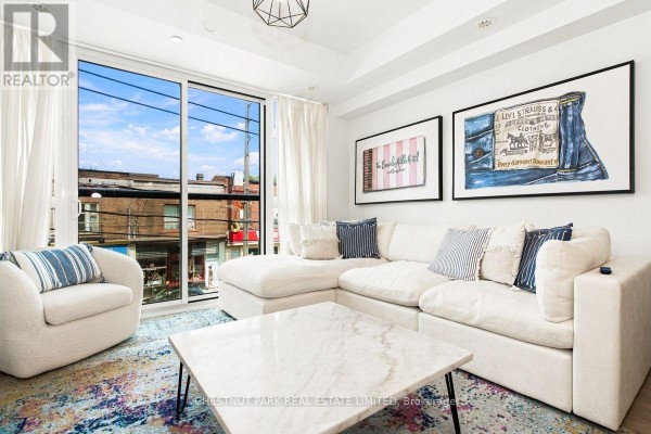 Living room with large windows, white furniture, and artwork on the walls. - 205 - 899 Queen Street E, Toronto