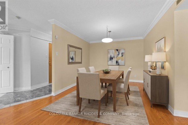 Dining room with light tan walls, hardwood floors, a wooden table, chairs, and a sideboard. - 205 - 939 North River Road, Ottawa
