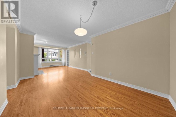 Living room with light tan walls, hardwood floors, a fireplace, a large window, and built-in shelves. - 205 - 939 North River Road, Ottawa