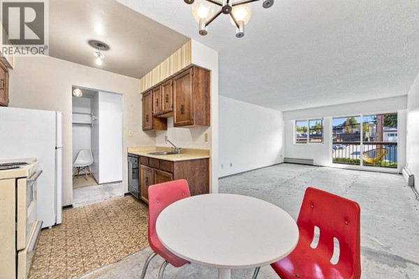 Kitchenette with dark wood cabinets and dining area with red chairs. - 205 1825 W 8th Avenue, Vancouver