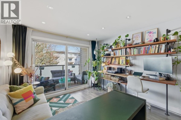 Living room with sofa, shelves filled with books and plants, and a desk with computer. - 205 1864 Frances Street, Vancouver