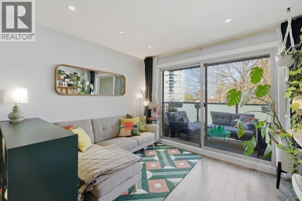 Living area with grey sectional sofa, patterned rug, and balcony view with outdoor furniture. - 205 1864 Frances Street, Vancouver