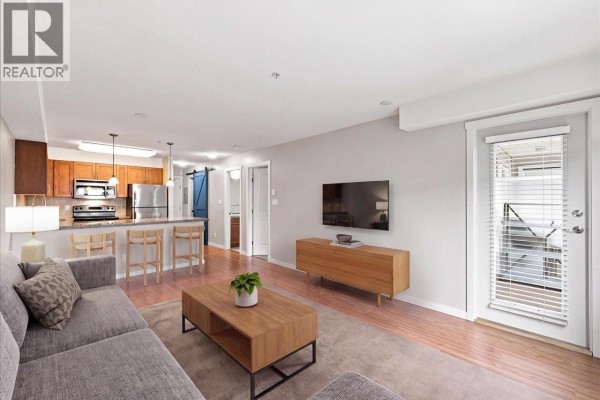 Living room and open-concept kitchen with a sofa, television, and kitchen island with bar stools. - 205 2373 Atkins Avenue, Port Coquitlam