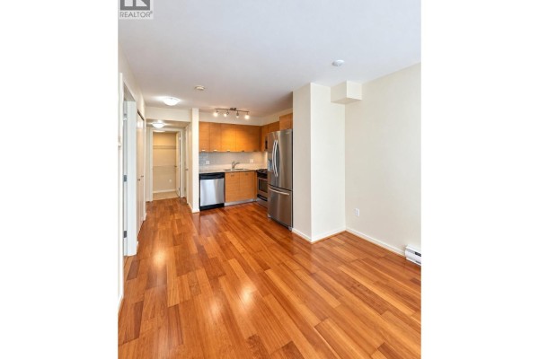 Open-concept apartment living space and kitchen with hardwood floors, light walls, and stainless steel appliances. - 205 2482 Spruce Street, Vancouver
