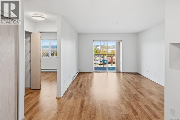 Empty living room and dining area with wood floors and balcony access. - 205 4971 Songbird Pl, Nanaimo