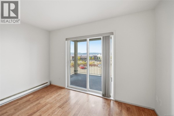 Bedroom with wood floors, a large sliding glass door to a balcony, and view. - 205 4971 Songbird Pl, Nanaimo