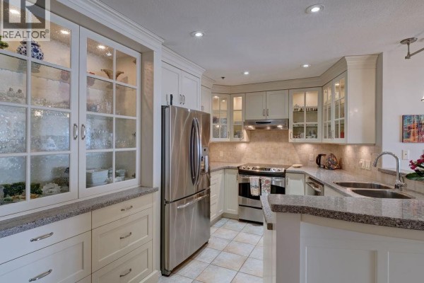 Kitchen view showing cream cabinets, granite countertops, stainless steel refrigerator, and a double sink. - 205 5470 Inlet Avenue, Sechelt