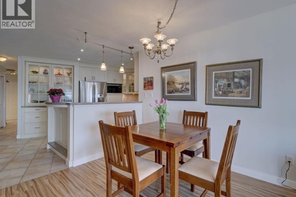 Dining area with a wooden table and four chairs, adjacent to the kitchen and living space. - 205 5470 Inlet Avenue, Sechelt
