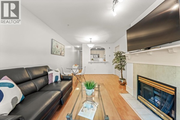Living area with fireplace, television, black sofa, and a view to the kitchen pass-through. - 205 5900 Dover Crescent, Richmond