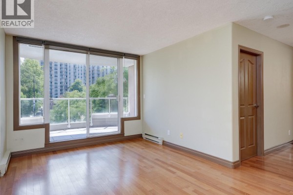 Living room with sofa, chairs, coffee table, television, and a balcony view. - 205 930 Yates St, Victoria