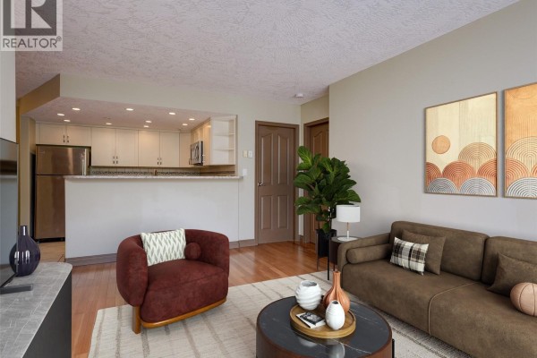 Living area with hardwood floors, beige walls, and an open kitchen with stainless steel appliances. - 205 930 Yates St, Victoria