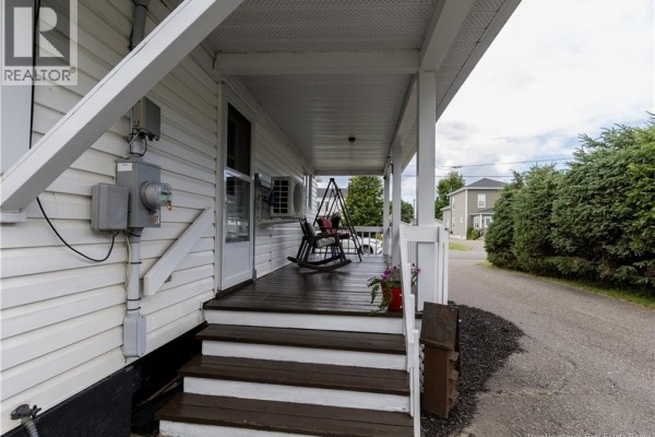 Side view of the white house exterior with black shutters, a covered porch, and a wooden deck. - 205 Basin Street, Grand Falls