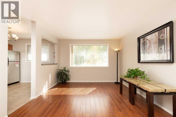 Living room with wood floors, large window, and view into the kitchen area. - 205 Columbia Boulevard W, Lethbridge