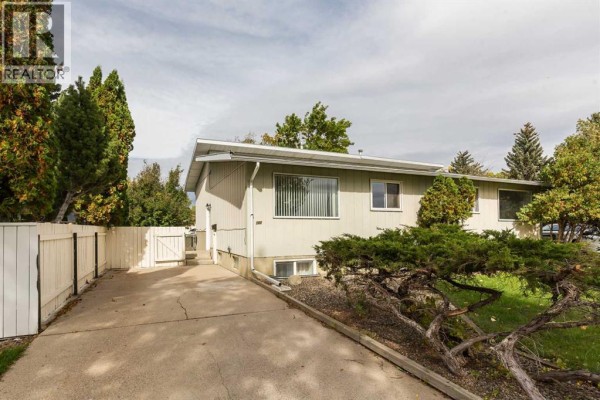 Exterior view of the duplex with a concrete driveway and a white picket fence. - 205 Columbia Boulevard W, Lethbridge