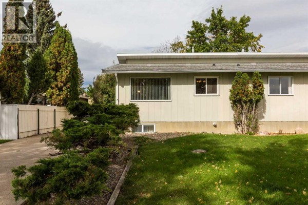 Side exterior view of the duplex showing siding, windows, and landscaping. - 205 Columbia Boulevard W, Lethbridge