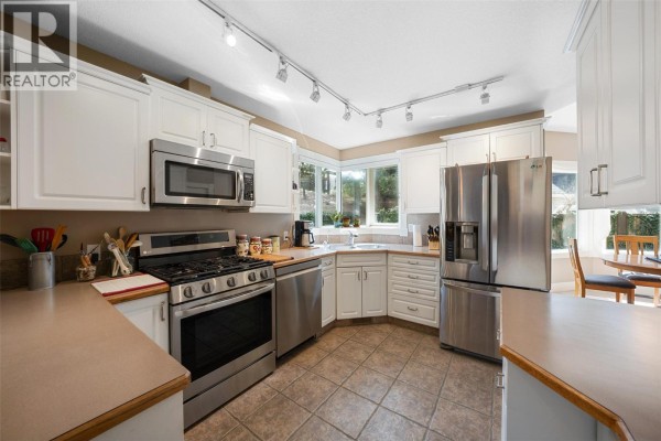 Kitchen with white cabinets, stainless steel appliances, and tile flooring. - 205 Merlin Court, Kelowna