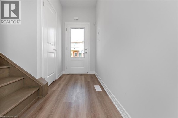 Interior view of a townhouse hallway with light grey walls, a staircase, and a glass-paneled back door. - 205 Thames Way Unit# 12, Mount Hope