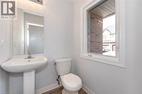 Powder room with a white pedestal sink, toilet, and a large window overlooking the street. - 205 Thames Way Unit# 12, Mount Hope